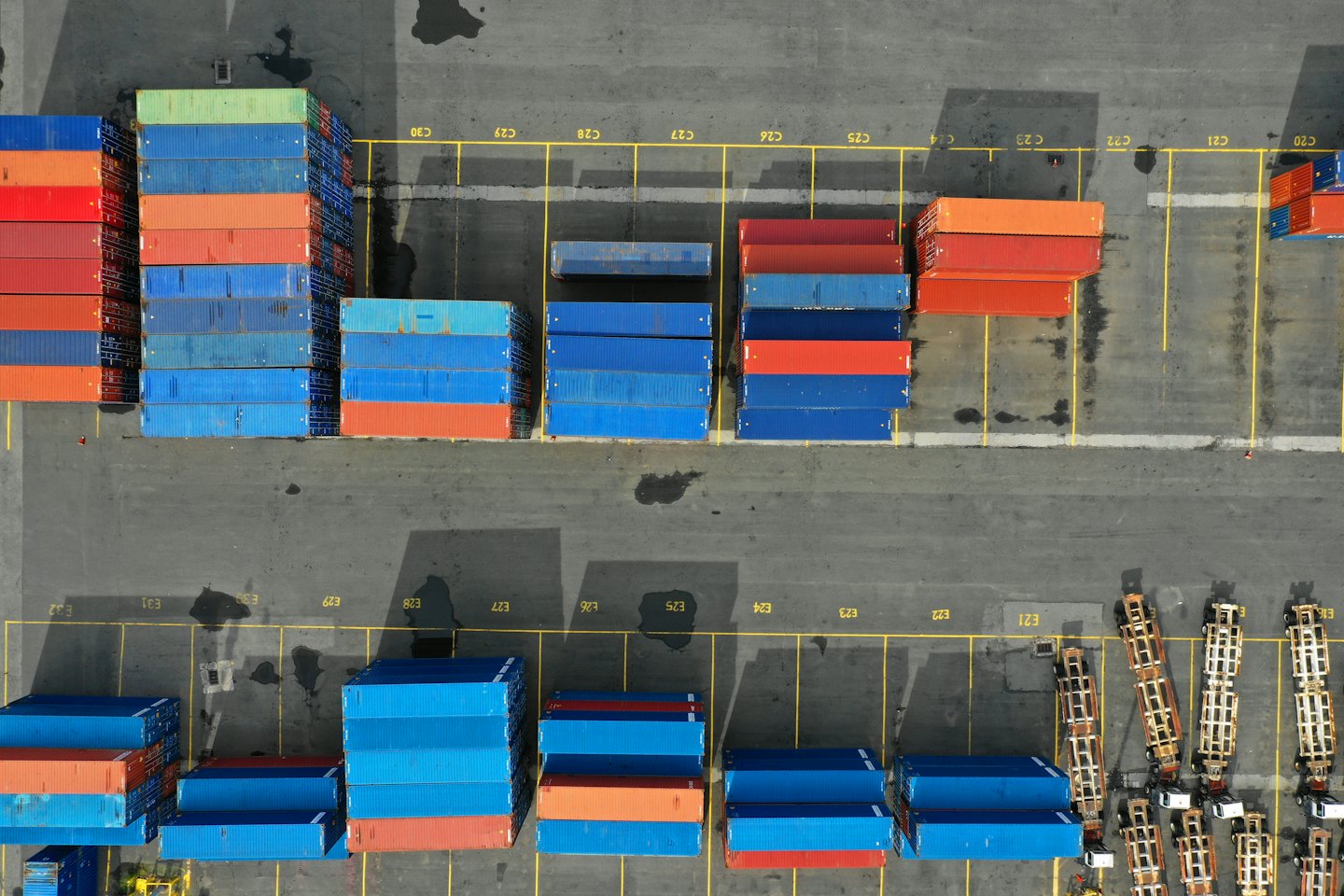 Vista aerea di un trafficato hub logistico con container marittimi blu e rossi impilati.